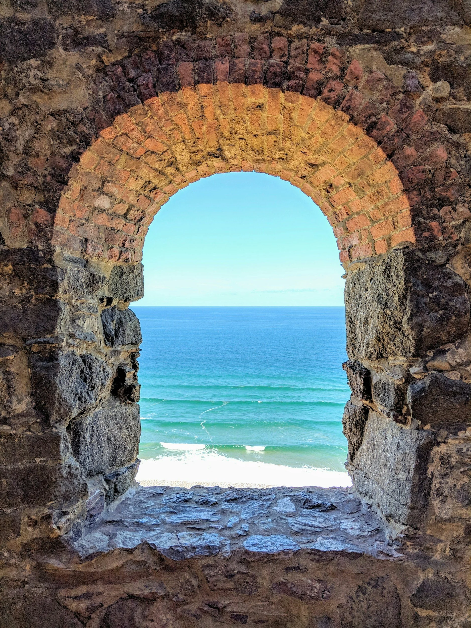 View of the ocean through a stone and brick arched window.