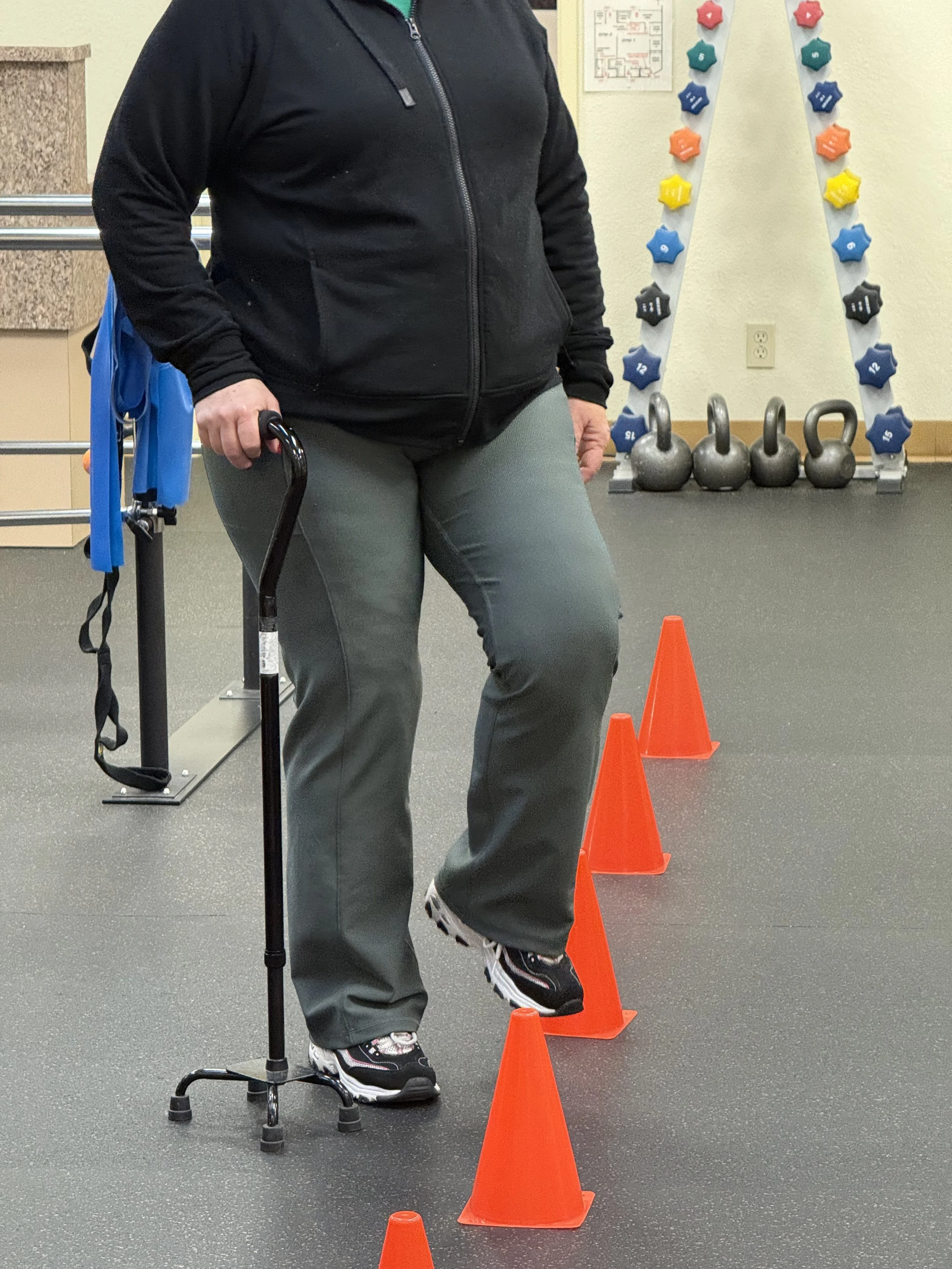 A fitness instructor leading a group exercise class with three participants performing squats in a bright, spacious studio with white walls and large windows.