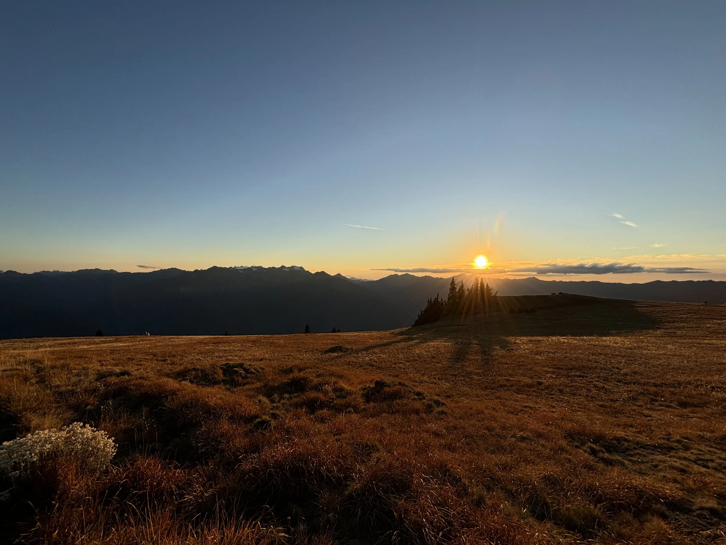 Sunset over a grassy hill with mountains in the distance and a clear sky.