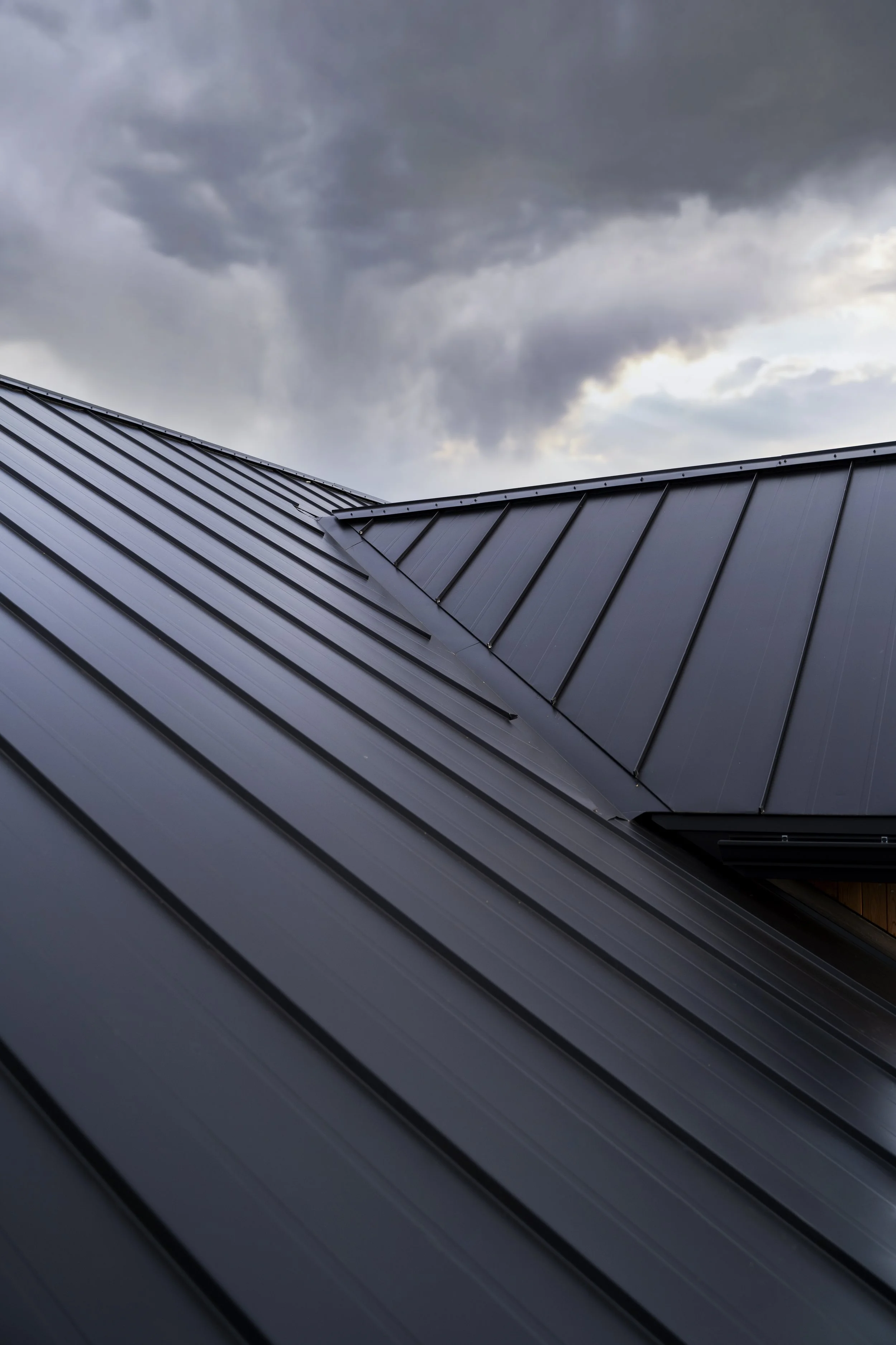 Close-up of dark gray metal roof panels with stormy clouds overhead.