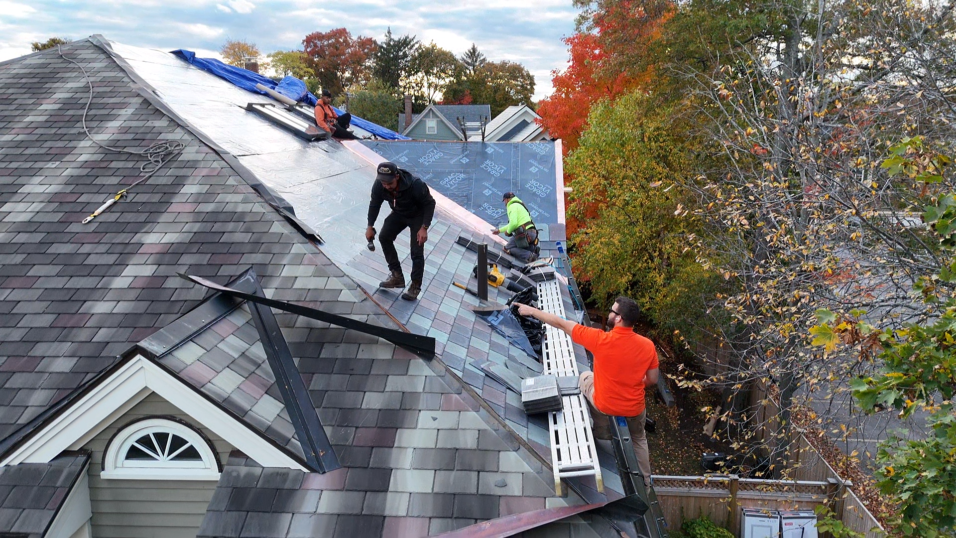 Workers installing new shingles and roofing materials on a residential house in an autumn setting.