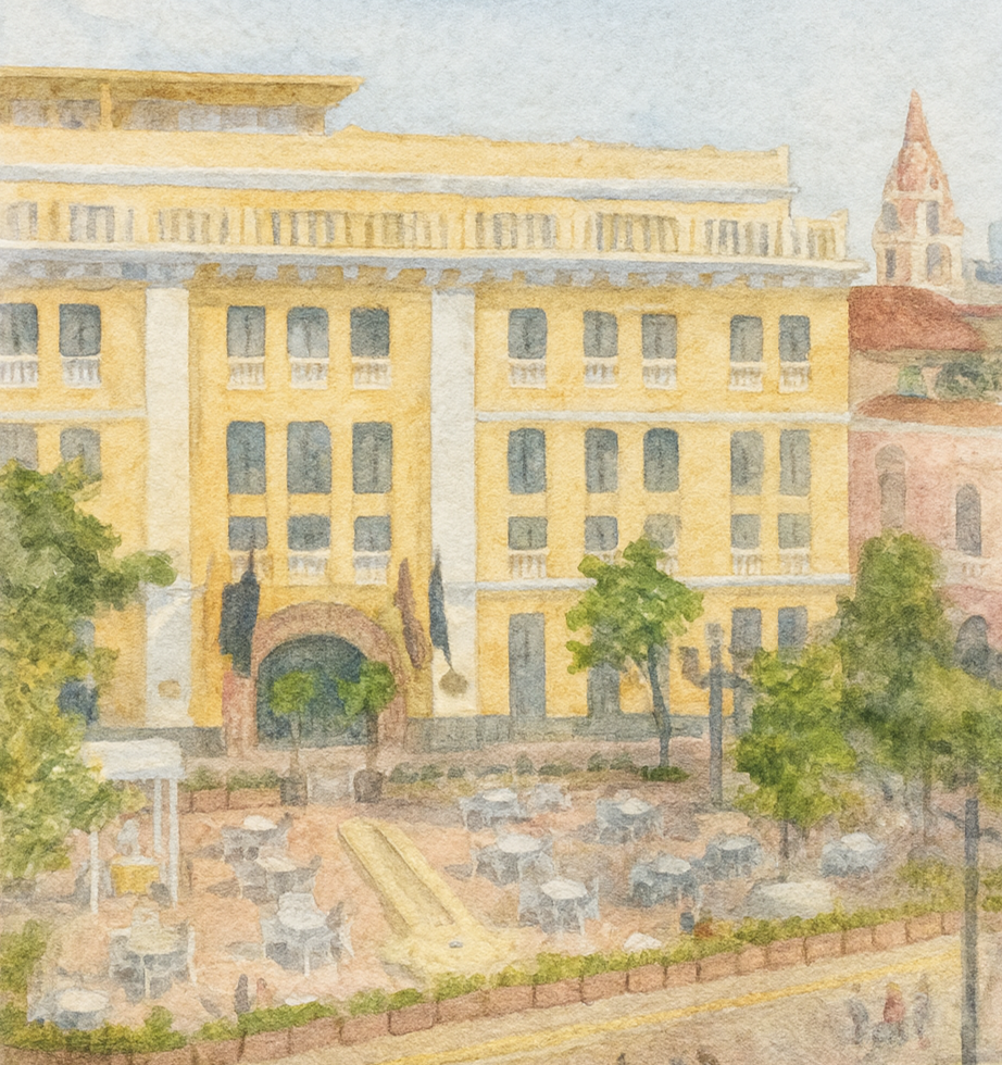 Watercolor painting of a yellow multi-story building with an arched entrance, surrounded by green trees and outdoor seating with tables and chairs. Urban setting with some neighboring buildings visible.