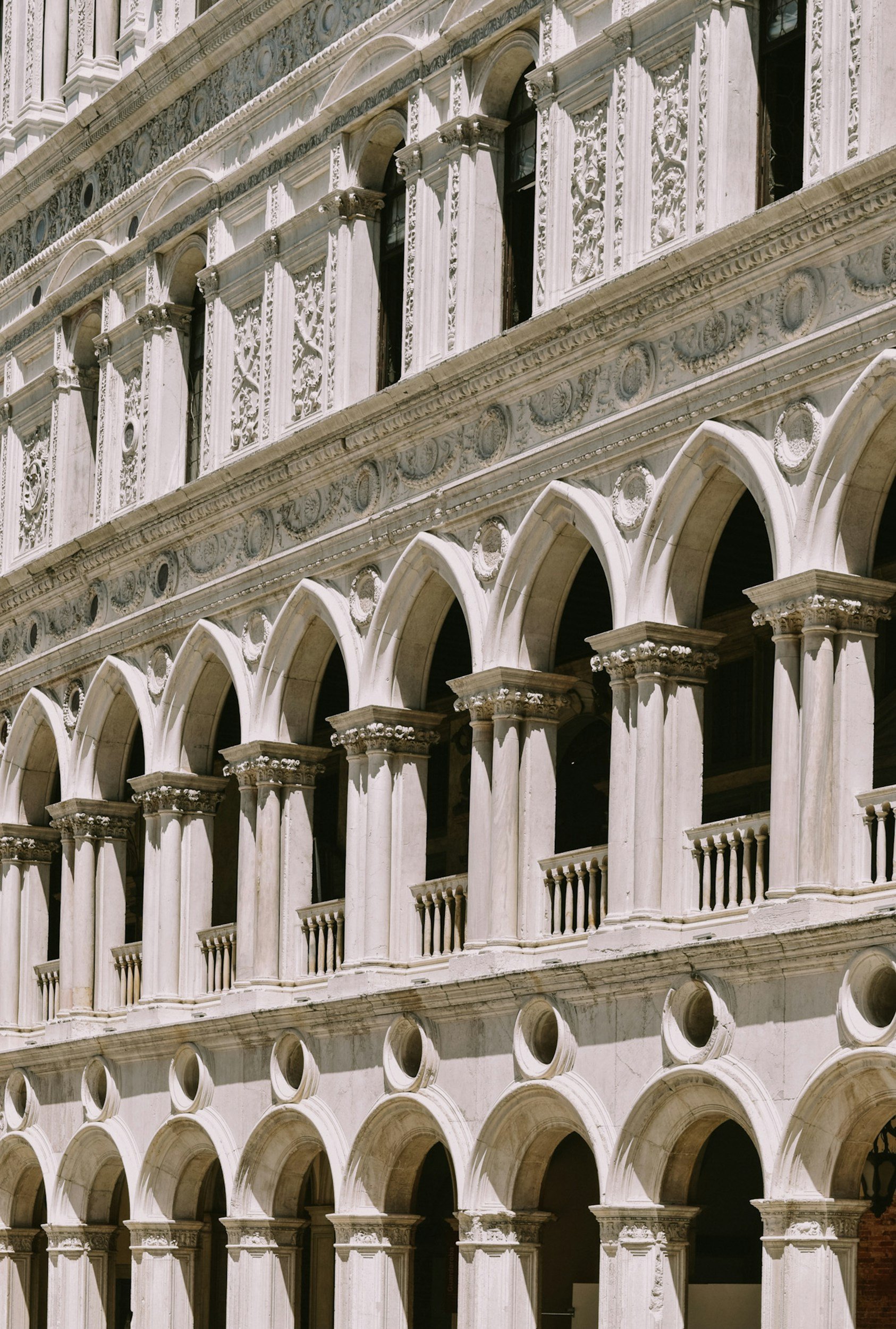 Close-up of a historic multi-story building facade with ornate architectural details, arches, columns, and decorative carvings, likely made of white marble or stone.