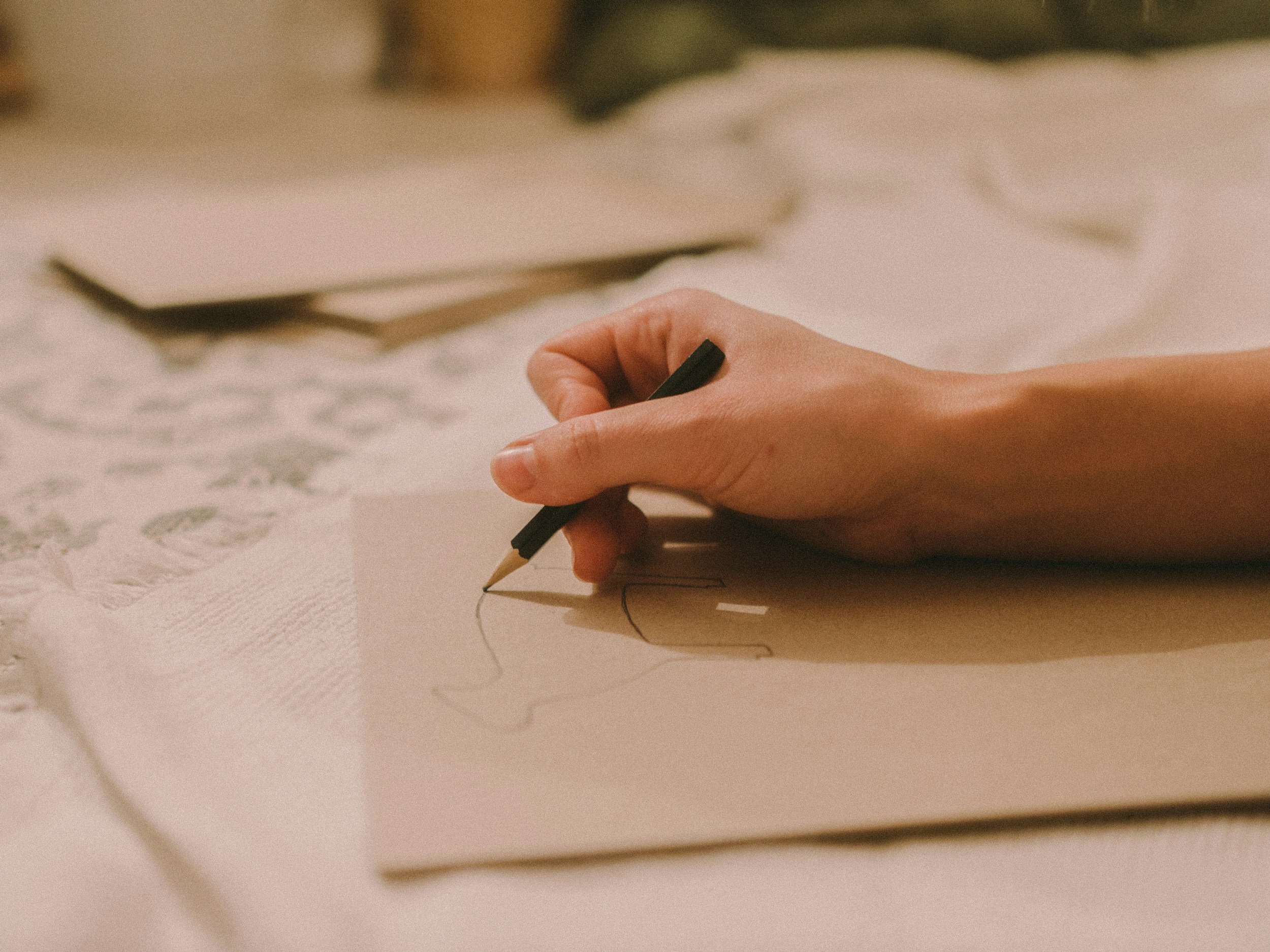 Close-up of a hand holding a black pen, drawing on a piece of paper with floral and lace patterns.