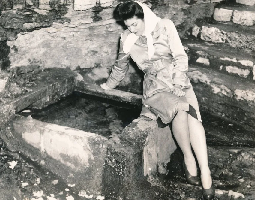 Old photograph of a woman looking down into a natural spring.