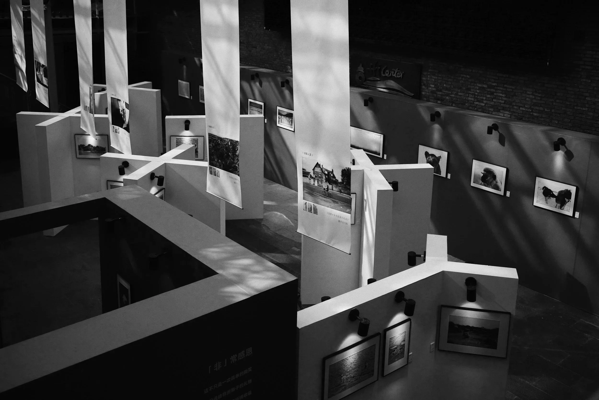 An art gallery with hanging banners and framed photographs on display walls, lit by track lighting.