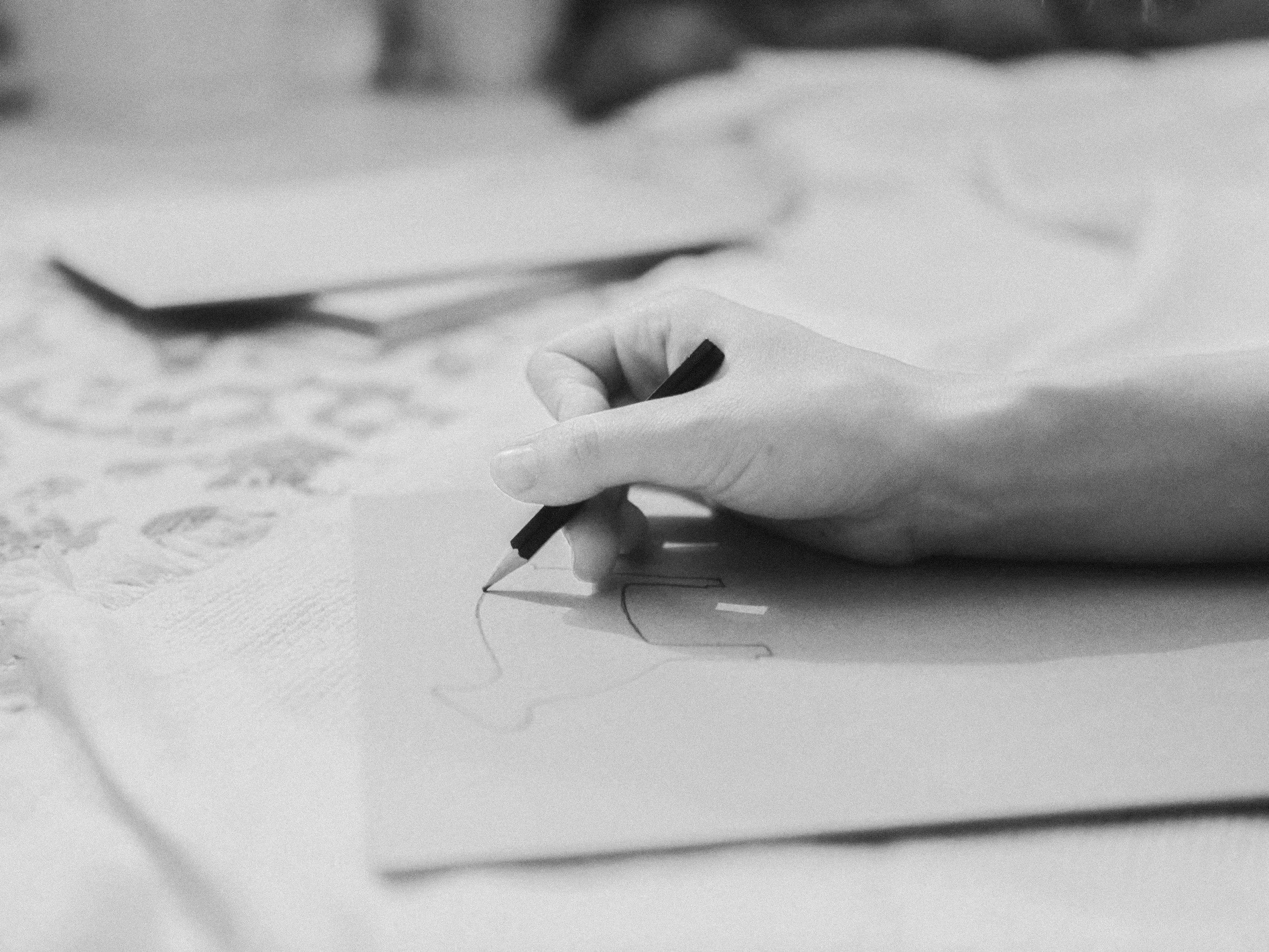 Close-up of a person's hand holding a pencil and drawing on paper with sketches or designs.