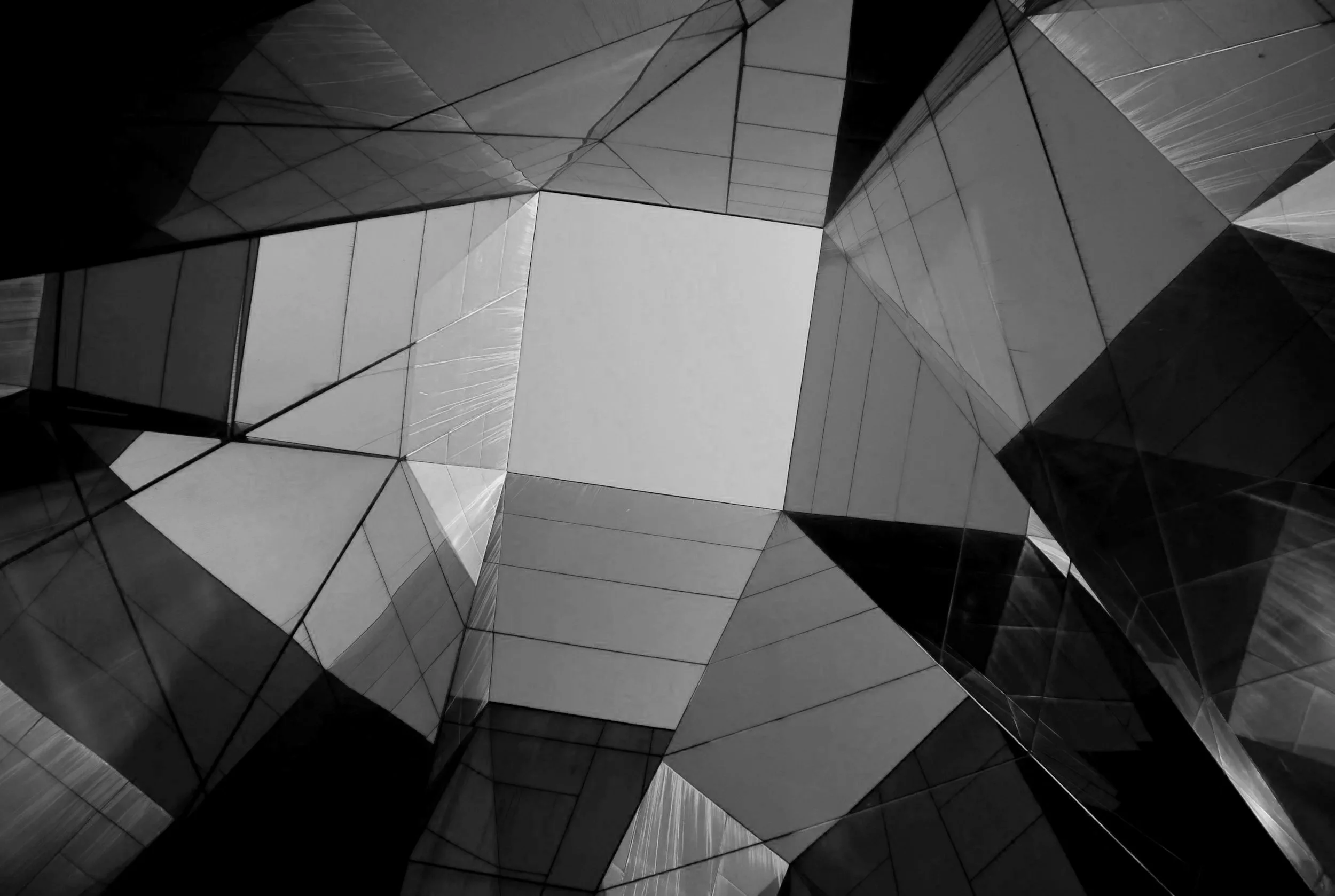 Abstract black and white architectural photograph of a modern building's glass and metal facade with angular shapes and reflections.