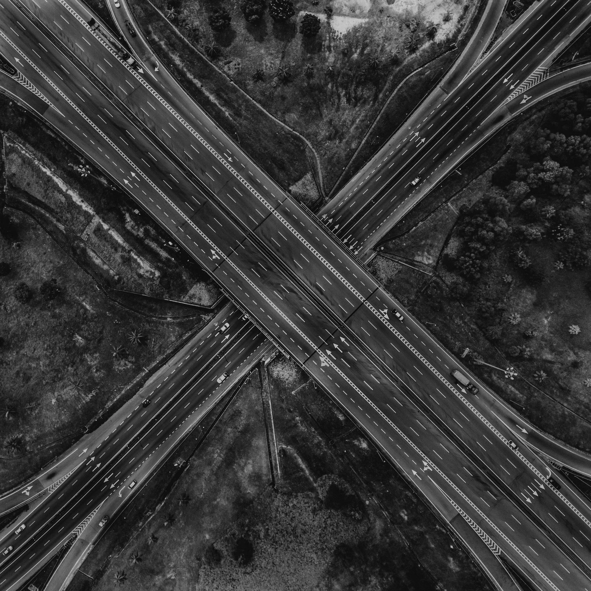 Aerial black and white photo of a multi-level highway interchange with roads curving and overlapping, surrounded by trees and open land.