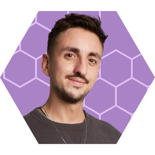 A man with short dark hair, facial hair, and a slight smile, wearing a dark shirt and a thin necklace, standing against a purple background with a hexagonal pattern and a bar graph in the bottom right corner.