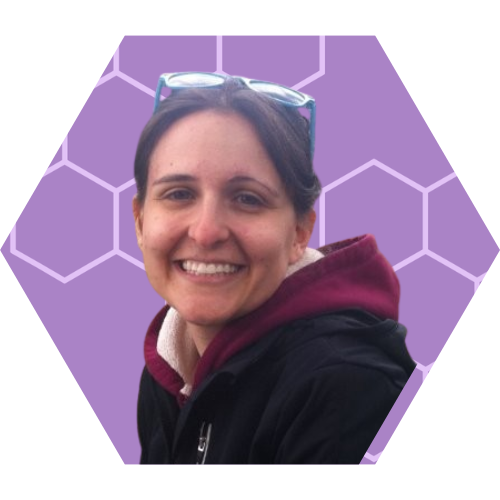 A woman smiling, wearing glasses on her head, a maroon hoodie, and a black jacket, against a purple background with hexagonal patterns.