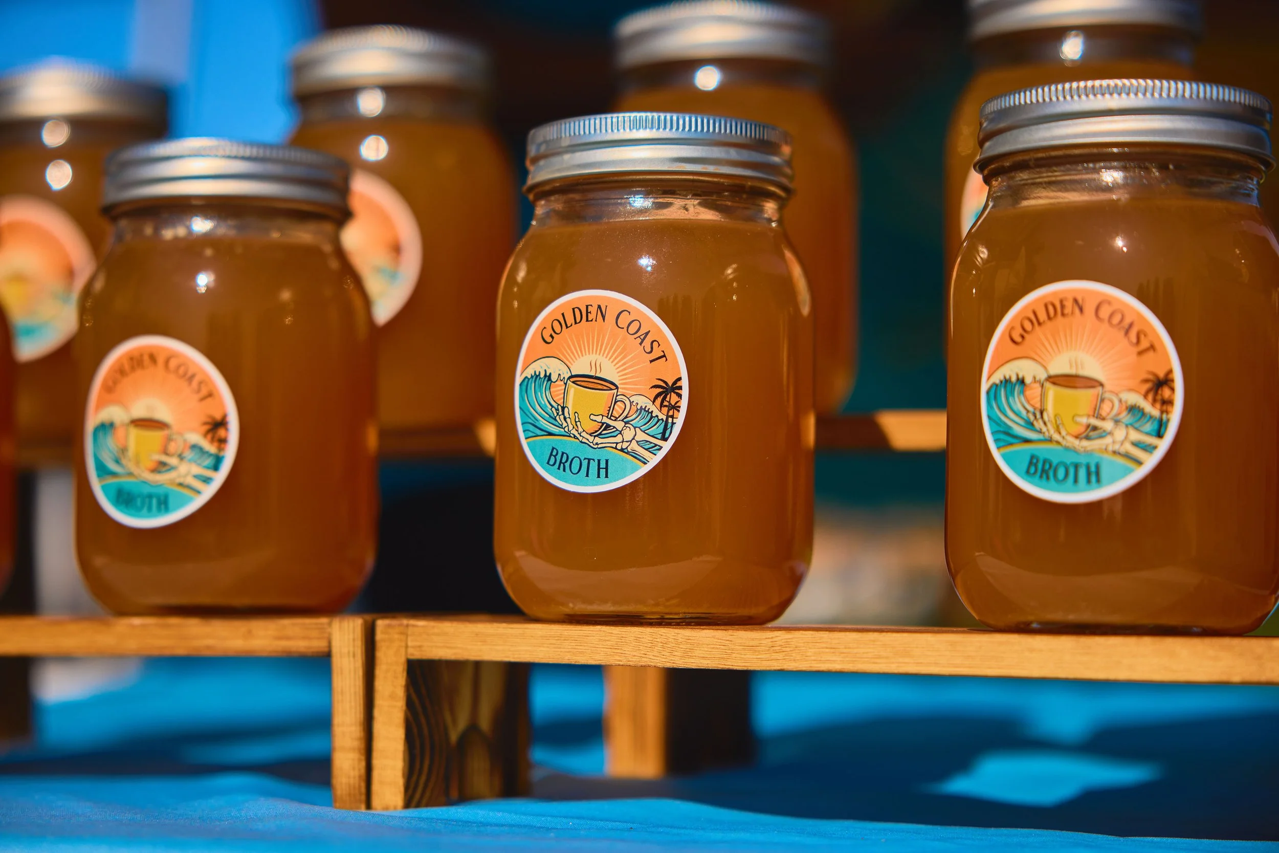 Glass jars labeled "Golden Coast Broth" arranged on a wooden shelf.