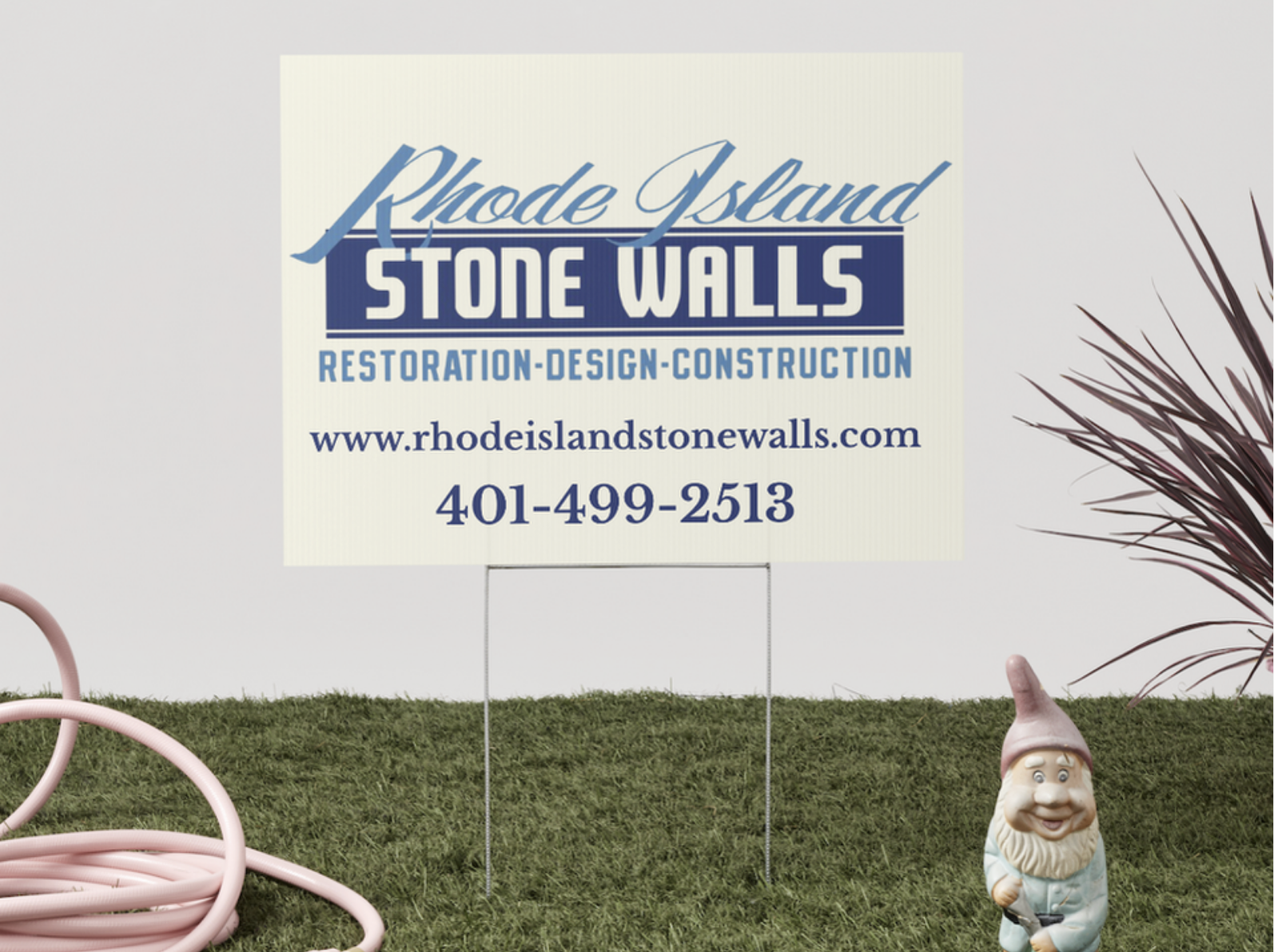 Sign for Rhode Island Stone Walls Restoration, Design, Construction with contact information, next to a garden gnome and a coiled pink garden hose.