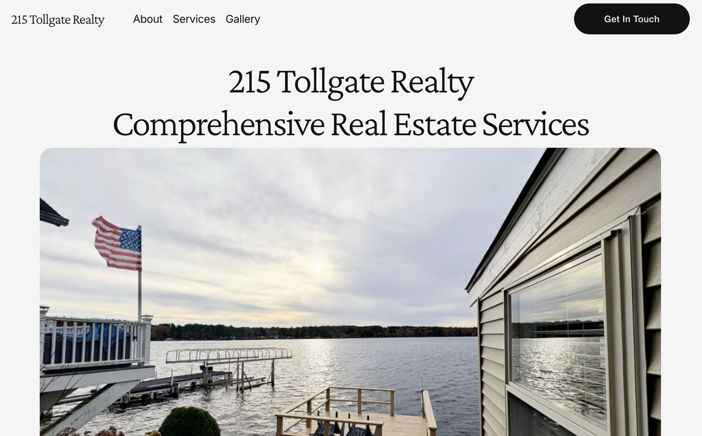View of a lake or river with a dock, American flag, and house with siding and window, under a cloudy sky.