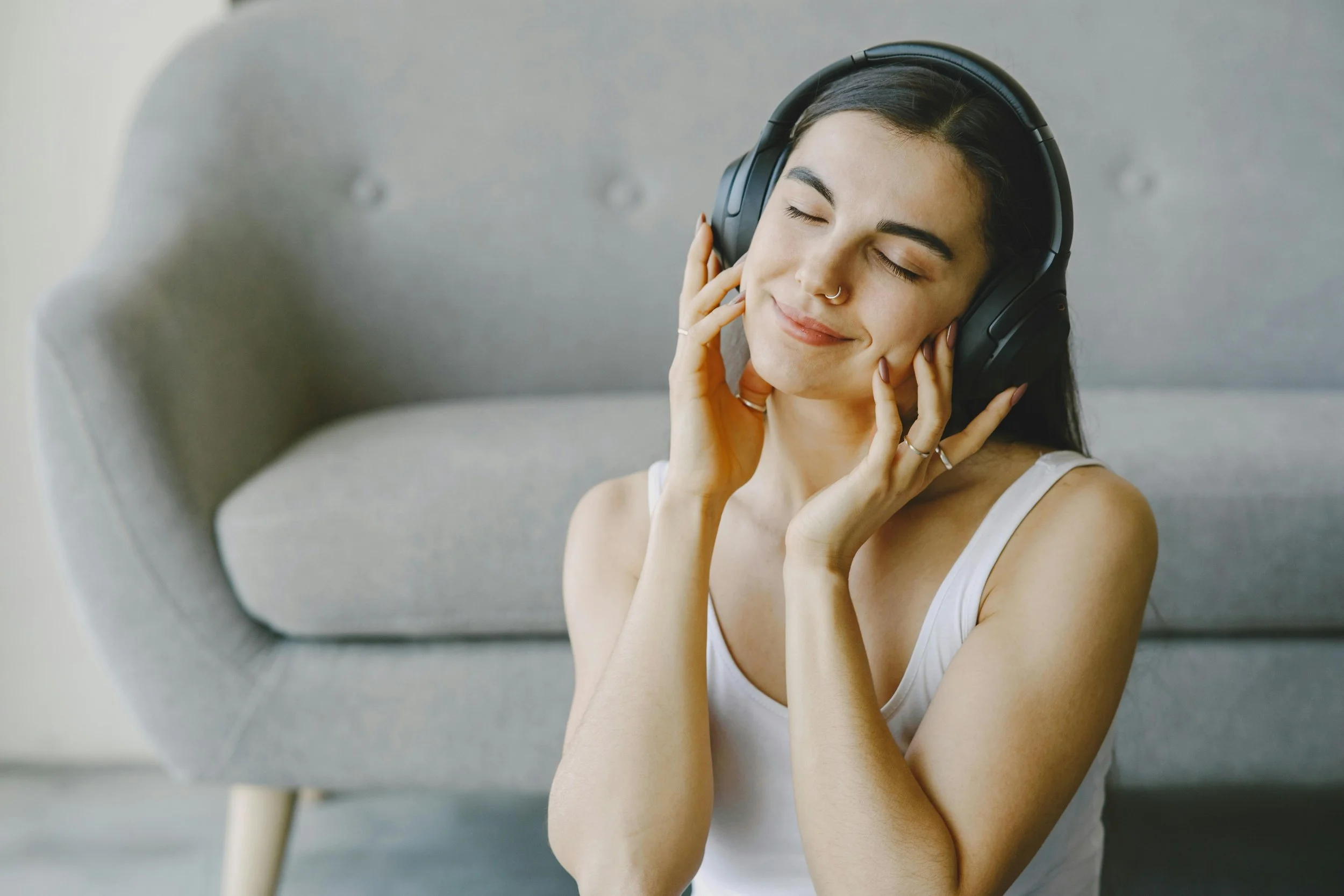 Woman lying down with headphones in a softly lit room, representing passive nervous system regulation through the Rest and Restore Protocol in Carmel-by-the-Sea.