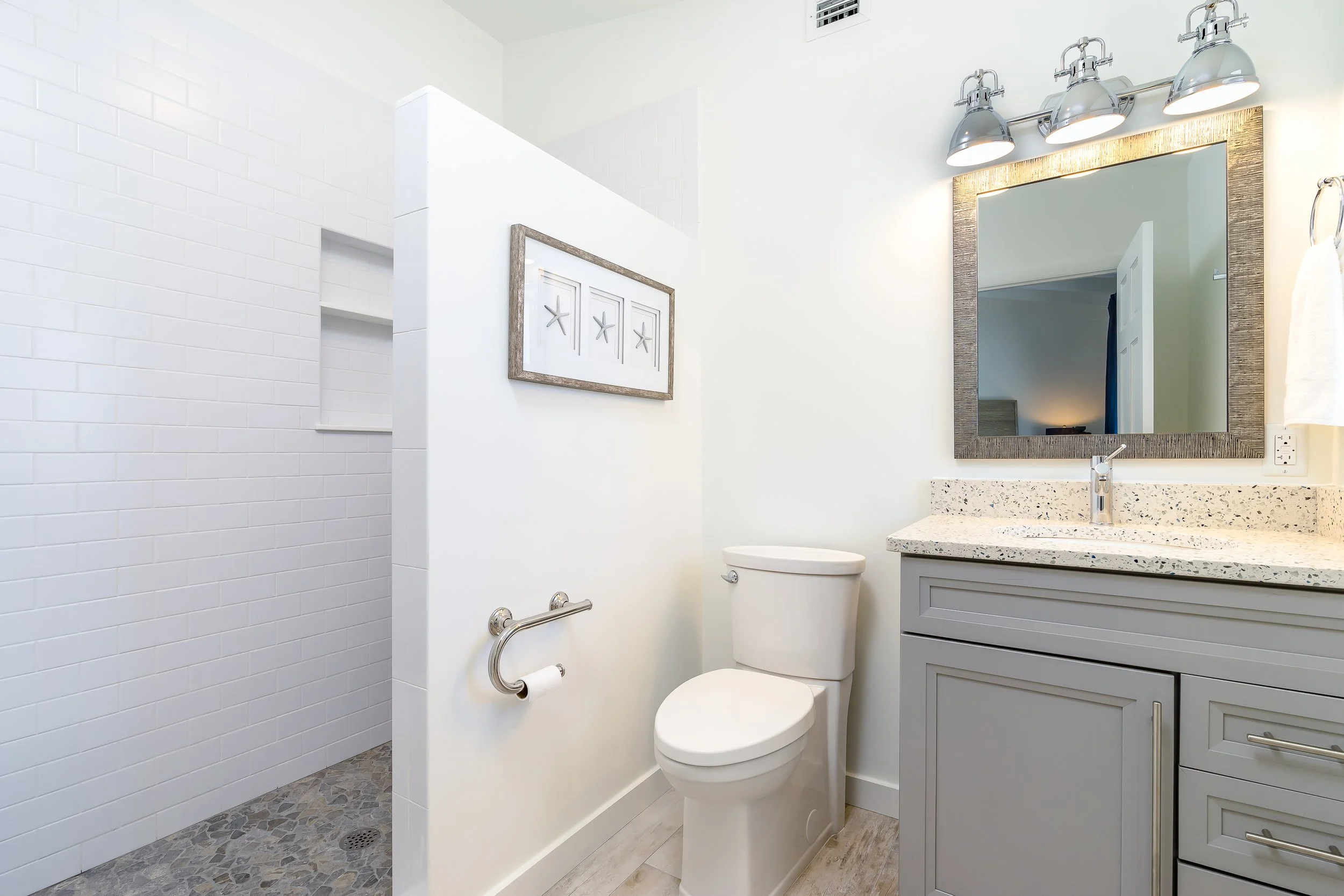 Modern bathroom with a toilet, vanity with a granite countertop, mirror, and a walk-in shower with white tile walls.