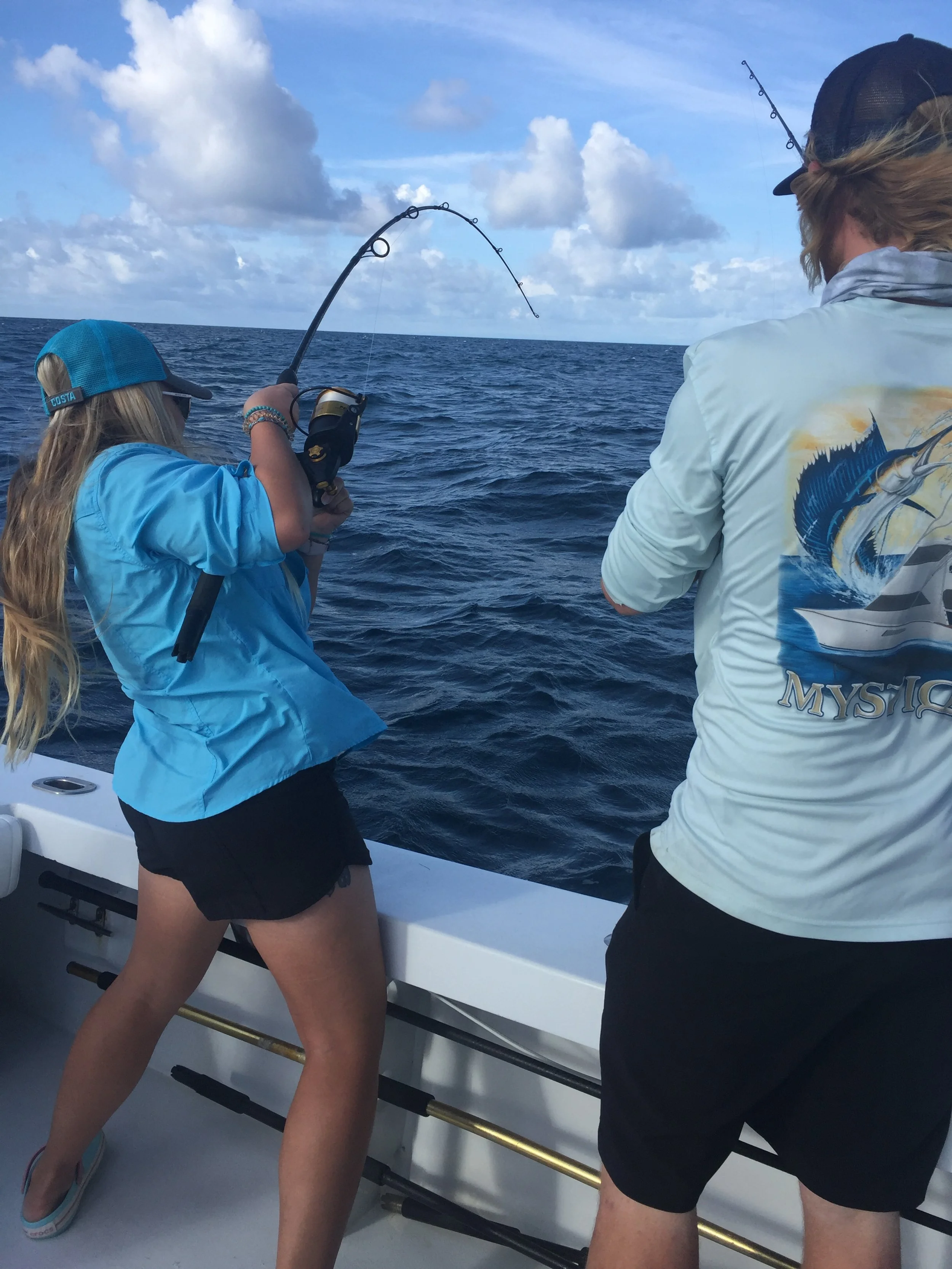Young girl fishing on a boat with an adult in the ocean under a partly cloudy sky.
