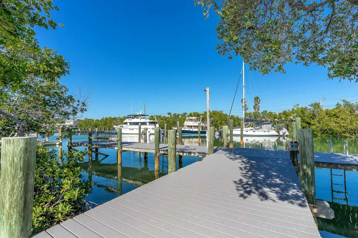 A marina with boats docked along wooden piers, surrounded by lush green trees under a clear blue sky.