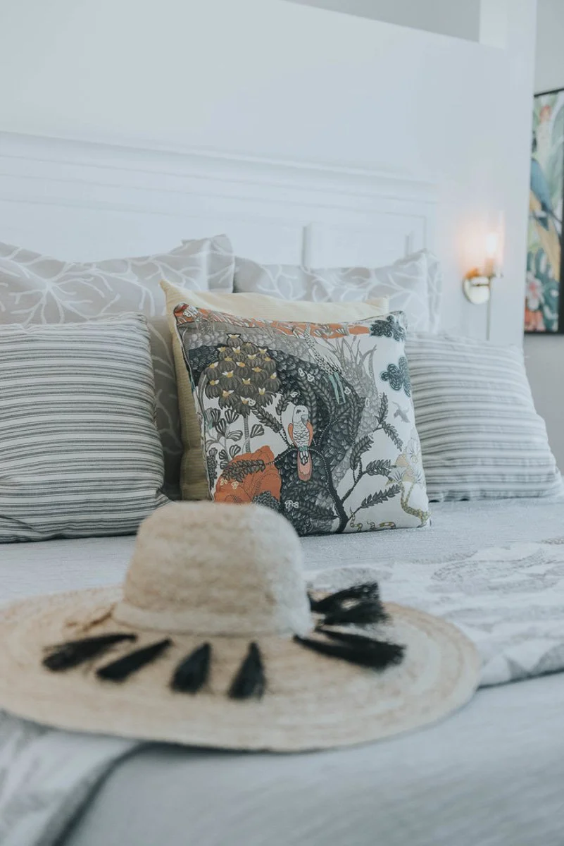A bed with patterned pillows and a straw hat with black tassels placed on it.