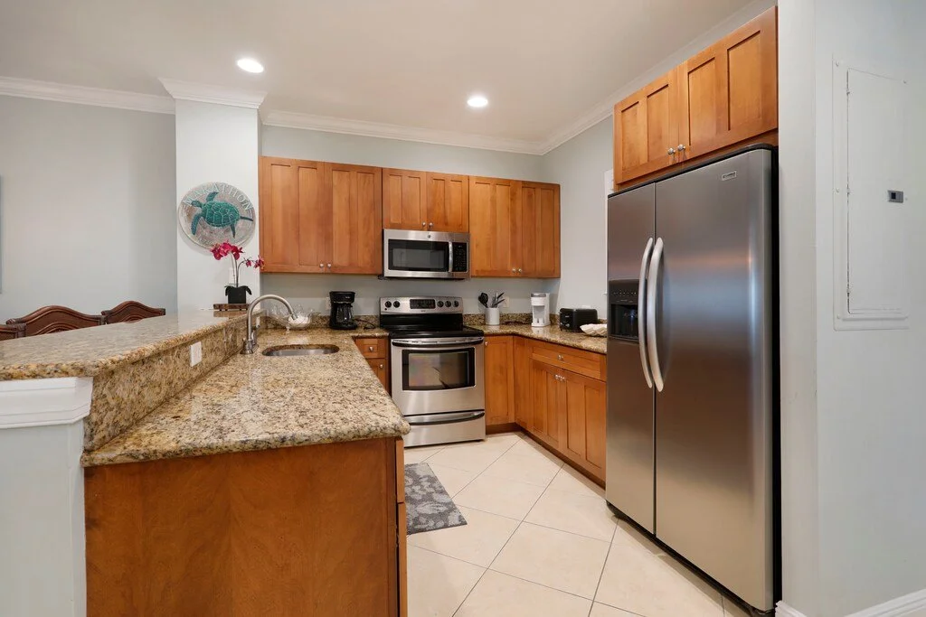 Kitchen with wooden cabinets, granite countertops, stainless steel refrigerator, microwave, oven, and various small appliances.