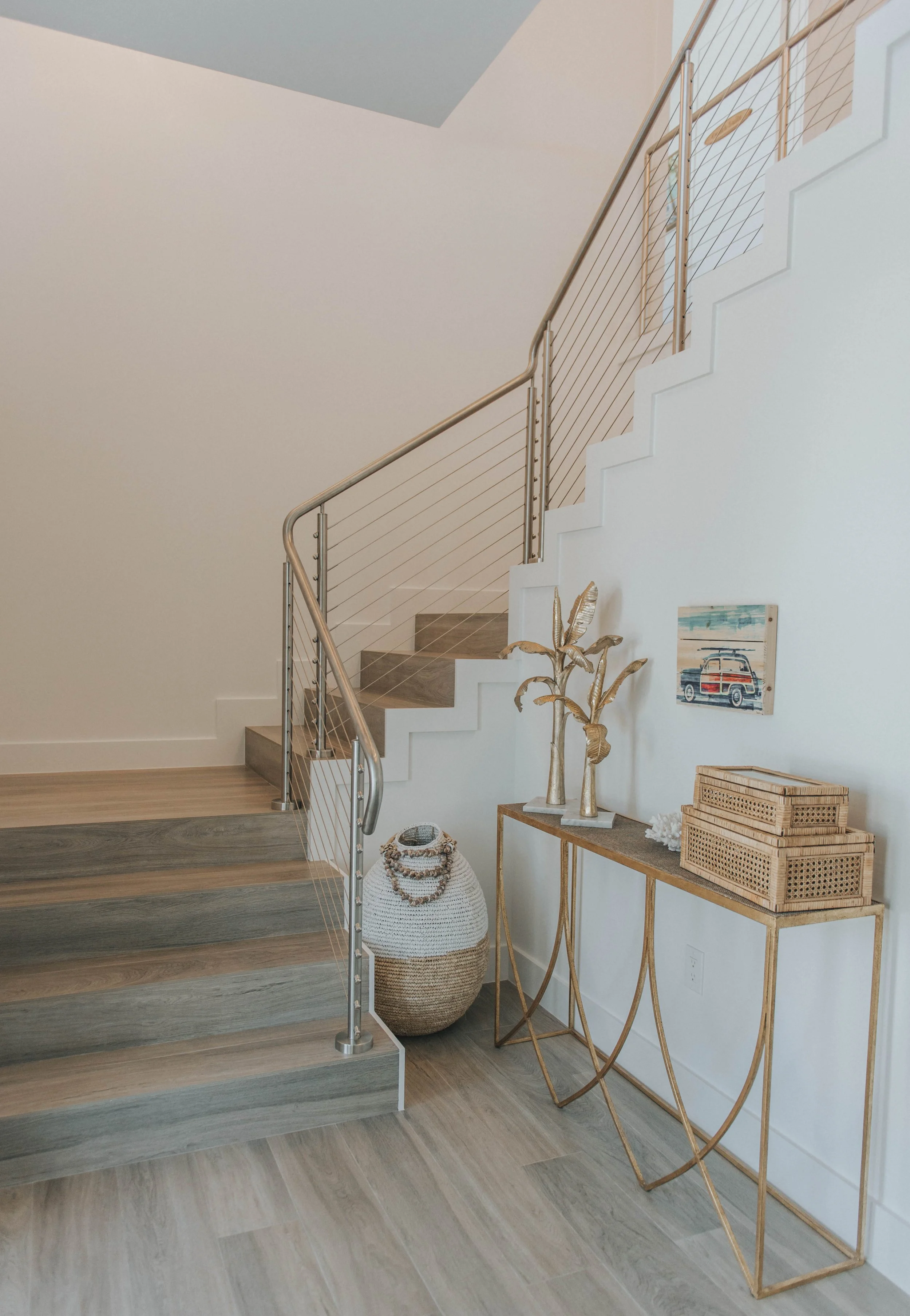 Interior corner of a home with a staircase, woven baskets, a gold decorative plant, and artwork on the wall.