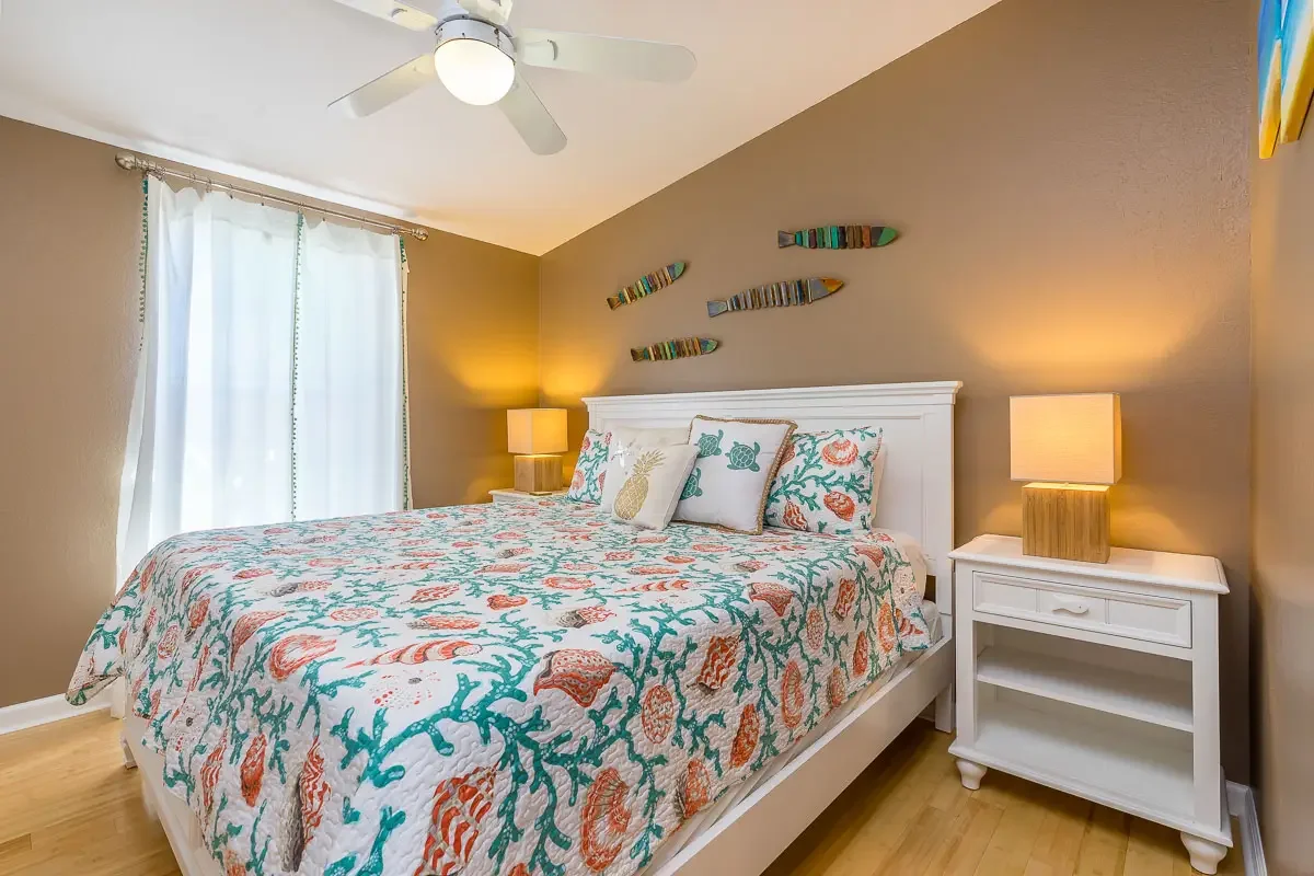 Beach-themed bedroom with patterned bedding, white headboard, beige walls, and ocean decor on the wall.
