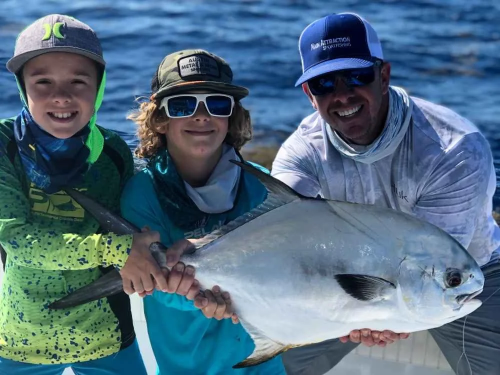 Three people holding a large fish on a boat with water in the background.