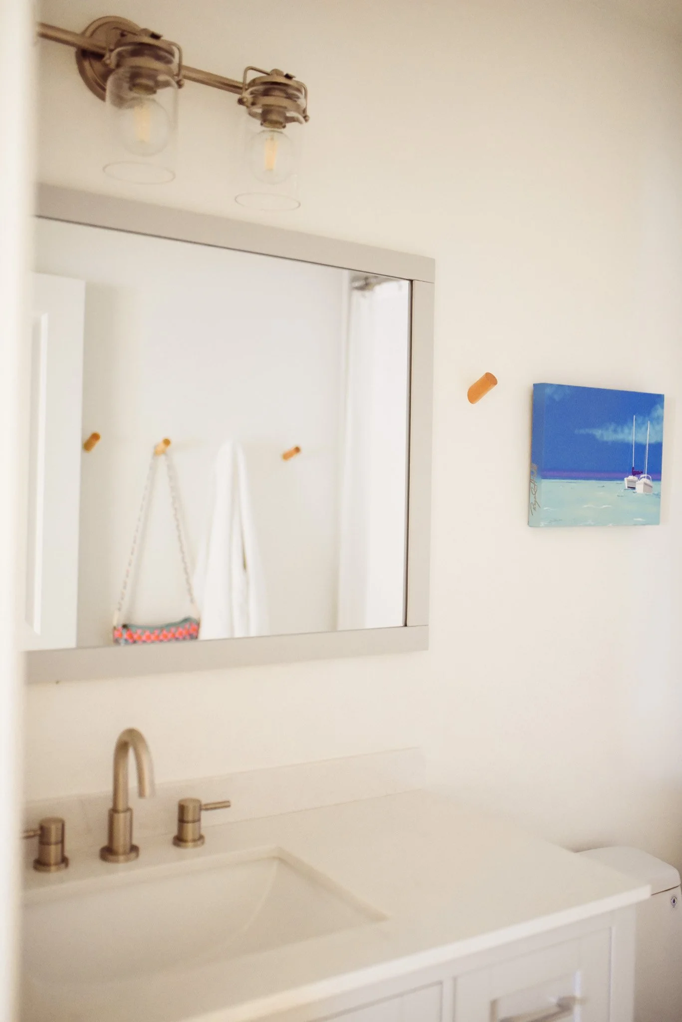 Bathroom with a silver-framed mirror, a hammer hanging on the wall, a painting of sailboats, and white fixtures.