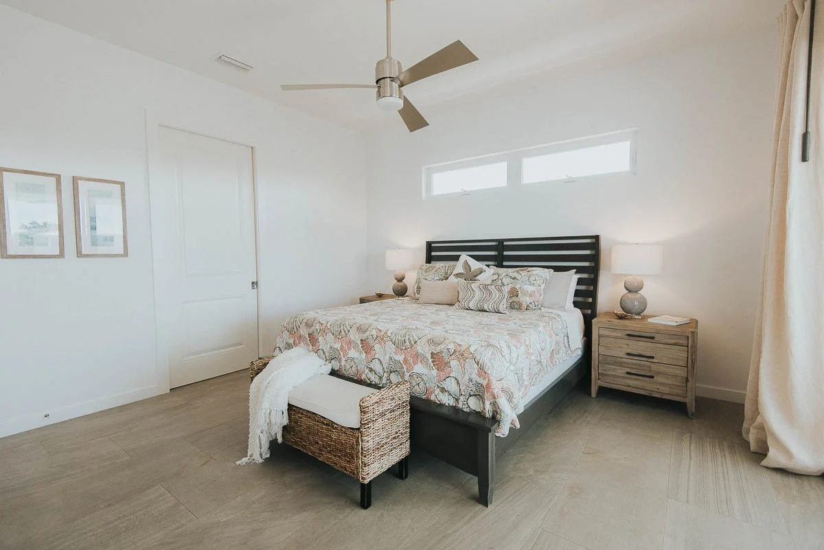 A bedroom with a large bed, nightstands with lamps, a ceiling fan, and light-colored flooring and walls.