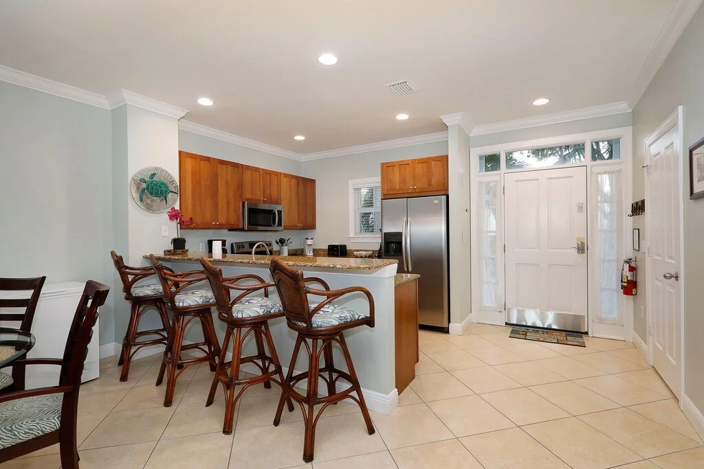 Kitchen with a breakfast bar, wooden cabinets, stainless steel refrigerator, microwave, and tiled floor.