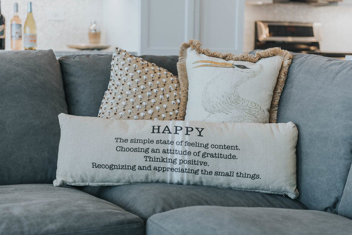 Decorative pillow on a gray sofa with an inspirational quote about happiness and appreciating small things.