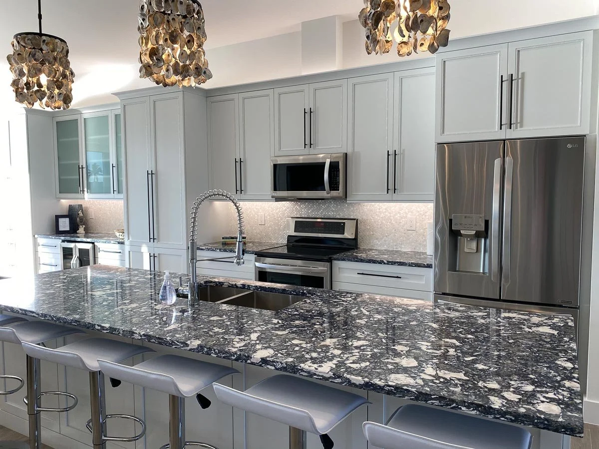 Modern kitchen with light gray cabinets, stainless steel appliances, marble island counter, and decorative pendant lights hanging from the ceiling.