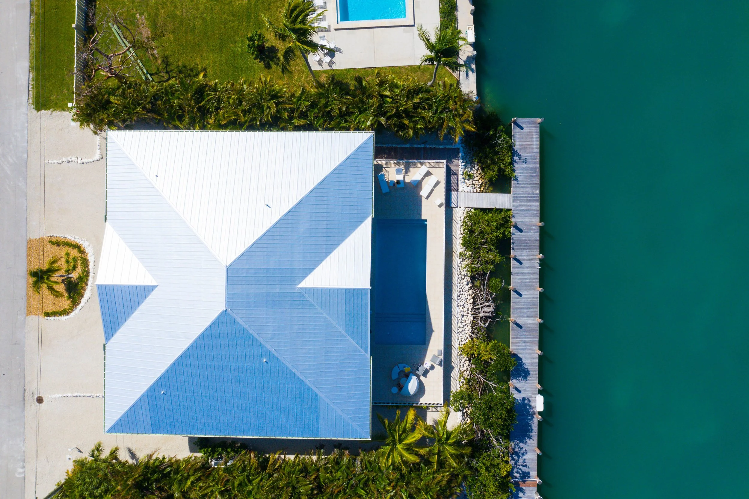 Aerial view of a house with a white metal roof, swimming pool, and a dock on the water.