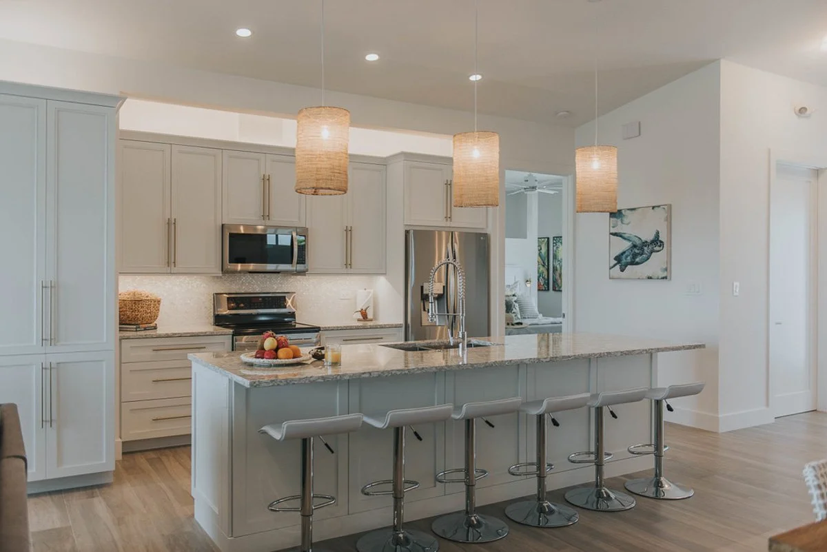 Modern kitchen with white cabinetry, granite countertops, and a central island with five bar stools. The kitchen features stainless steel appliances, pendant lighting, and a wooden floor.