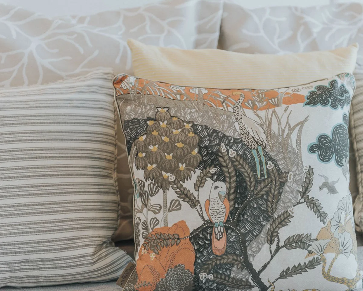 Decorative pillow with a nature scene featuring parrots, trees, and clouds on a white background.