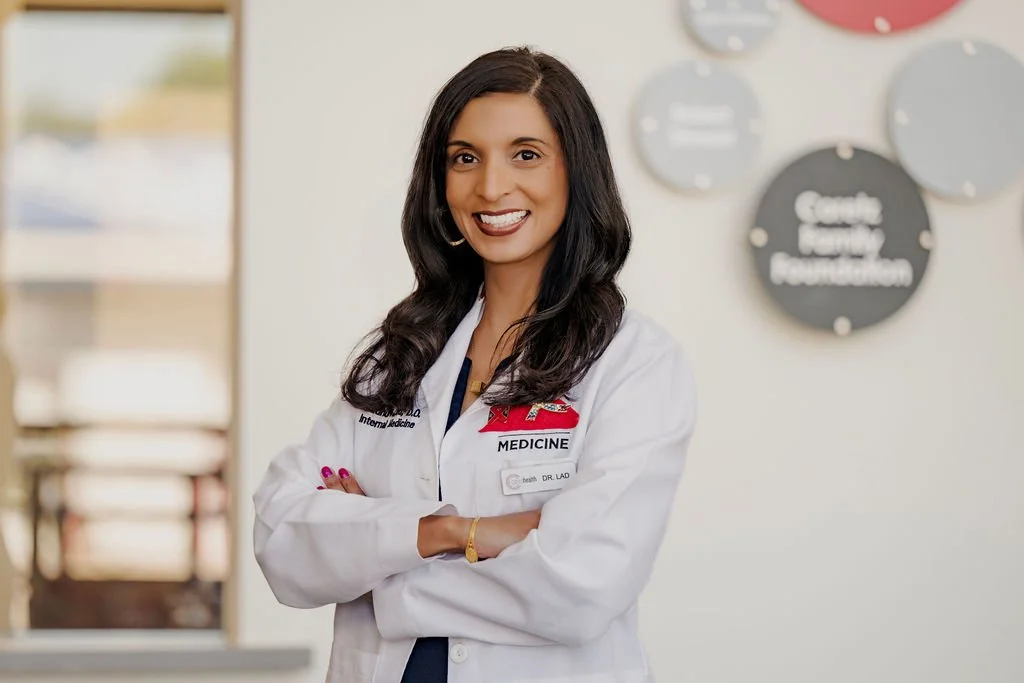 Dr. Lad wearing a white coat standing with arms crossed in a medical facility, smiling at the camera.
