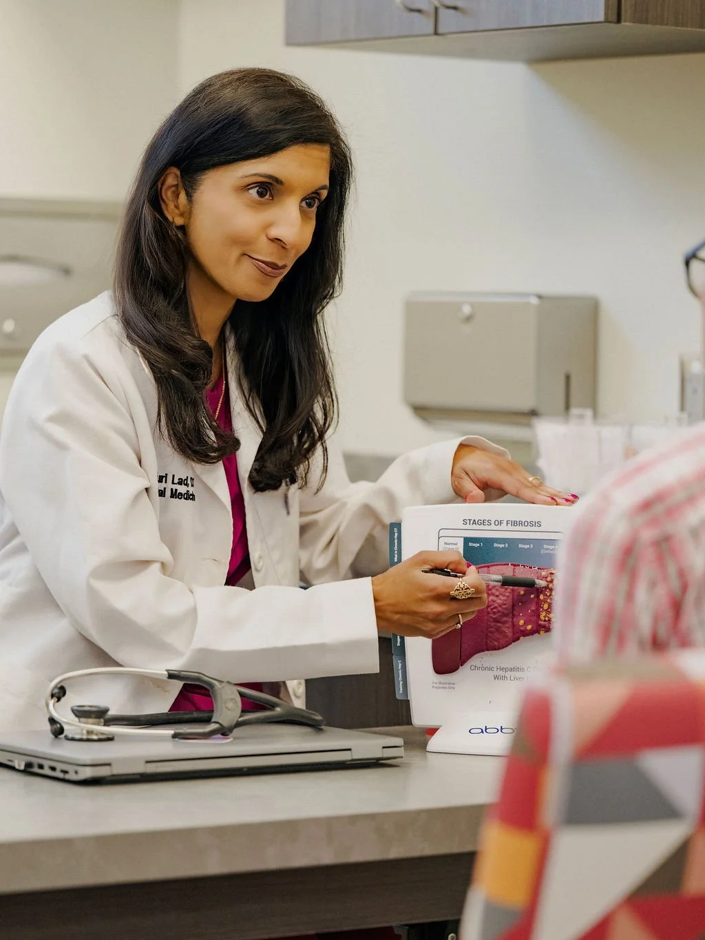 A female doctor showing a diagram of stages of fibrosis to a patient in a medical office.