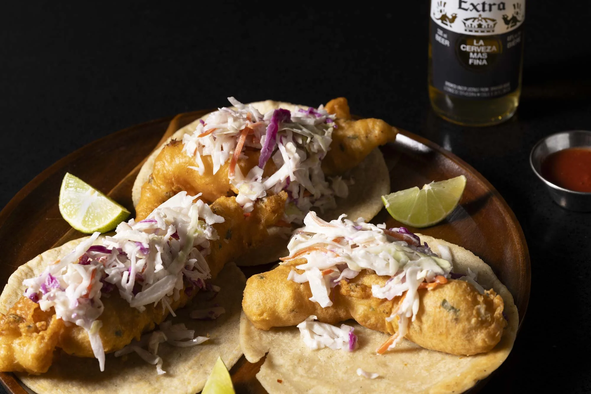 three fish tacos with a creamy coleslaw and limes