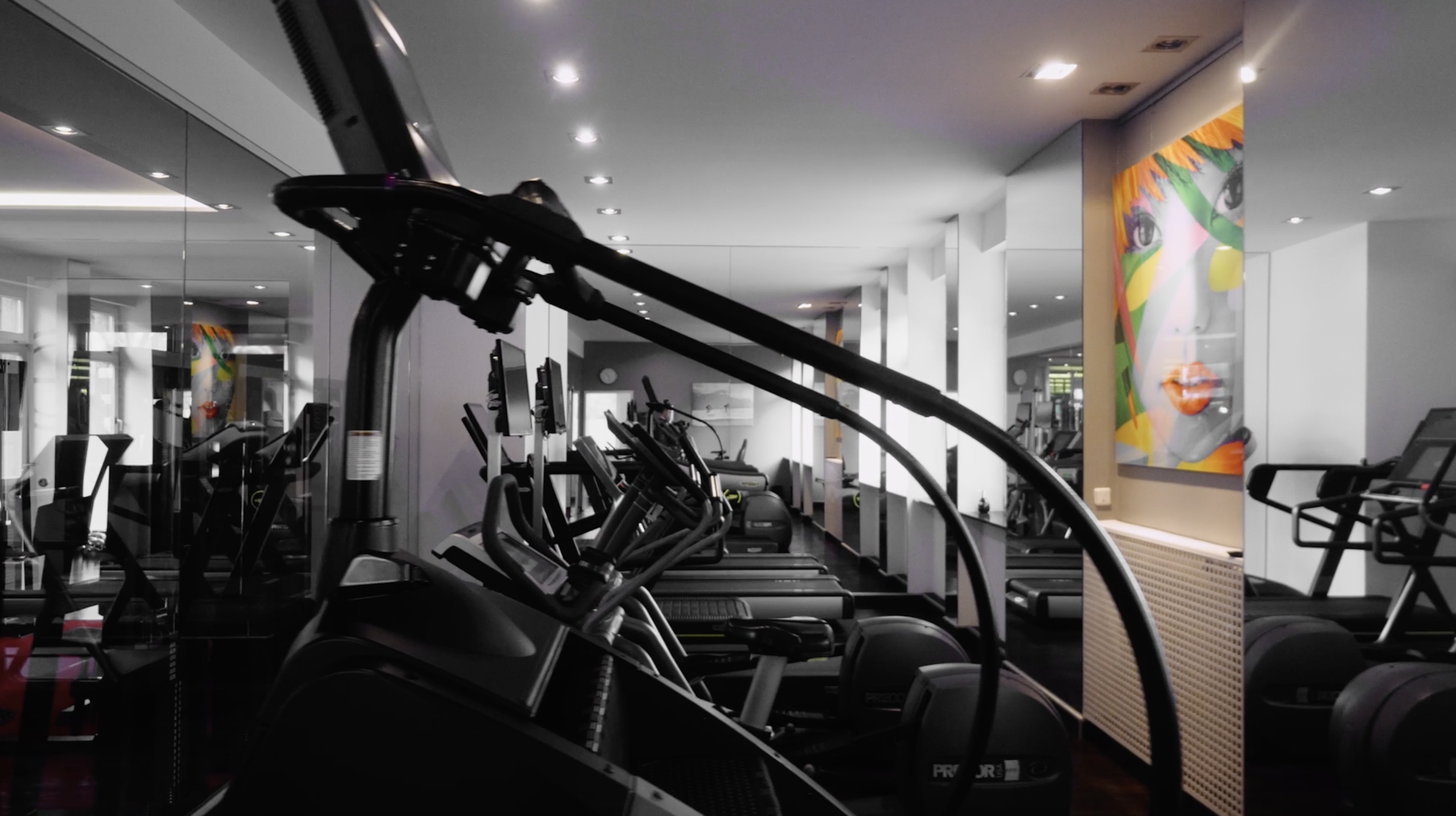 Empty gym with treadmills, elliptical machines, and a colorful portrait of a woman on the wall.