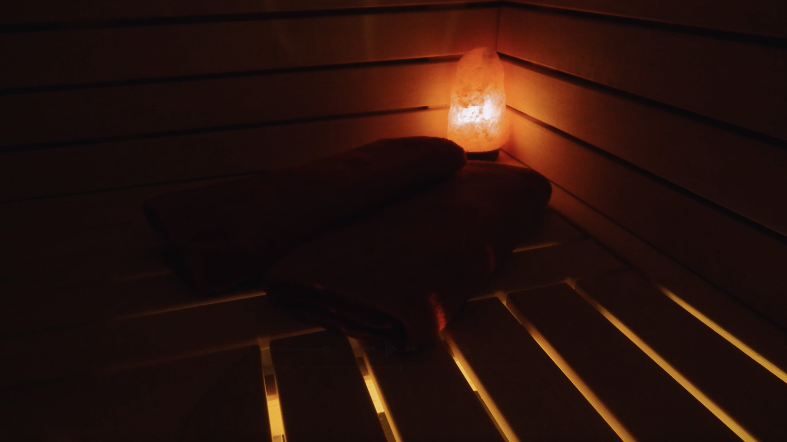 Salt lamp casting warm orange glow on a wooden shelf with folded towels.