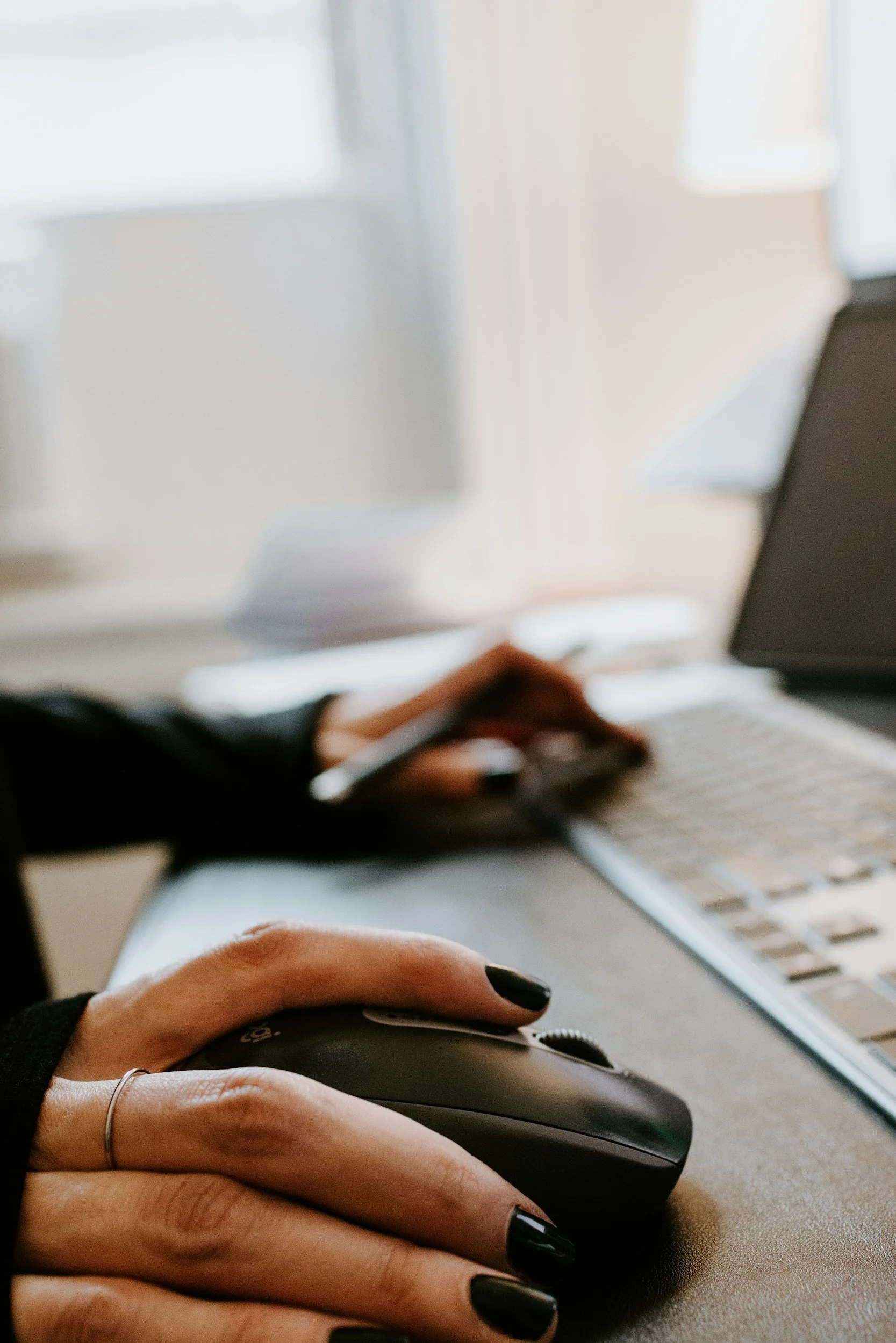 Close-up of a person’s hand on a computer mouse, with a keyboard and laptop in the background.