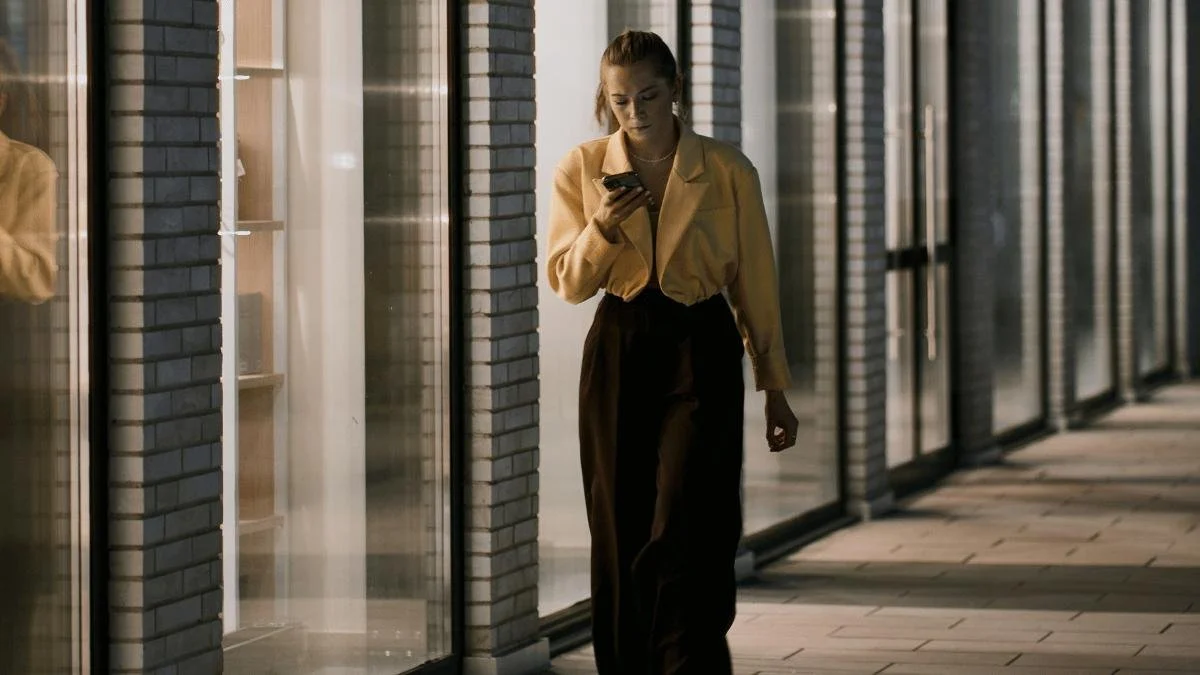 Woman walking down hallway staring down at her phone, always busy, rushing around