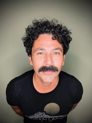 A man with curly hair and a mustache is smiling and looking at the camera.