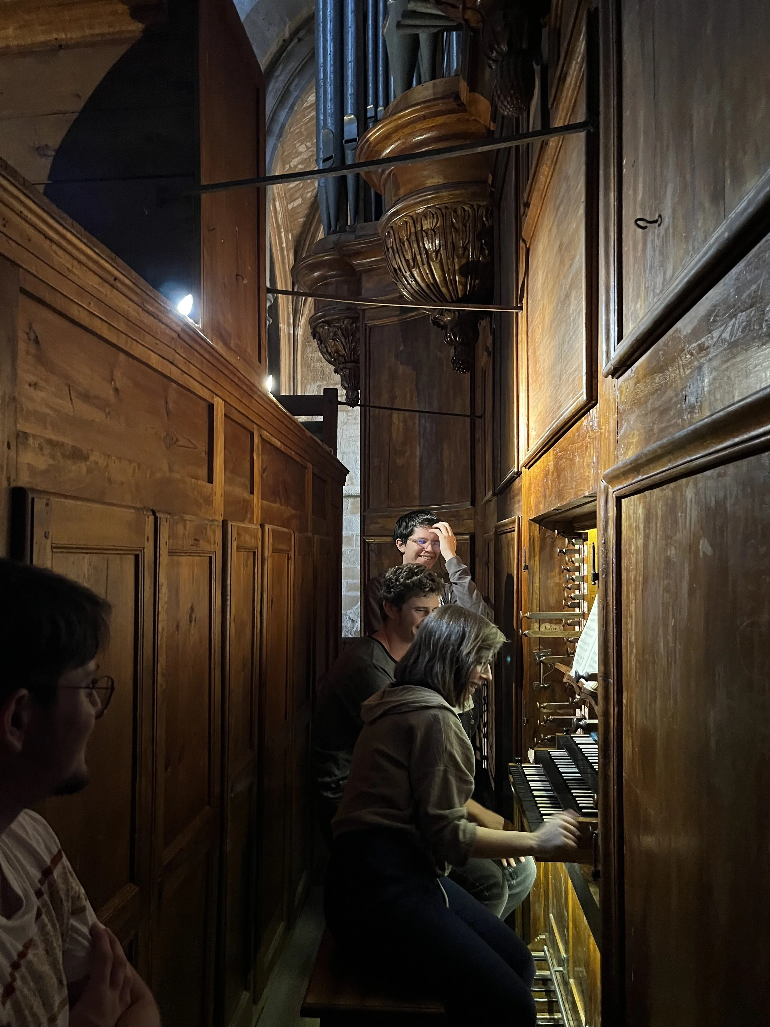 Groupe de personnes jouant de l'orgue dans une petite cabine en bois, probablement dans une église ou un lieu historique.