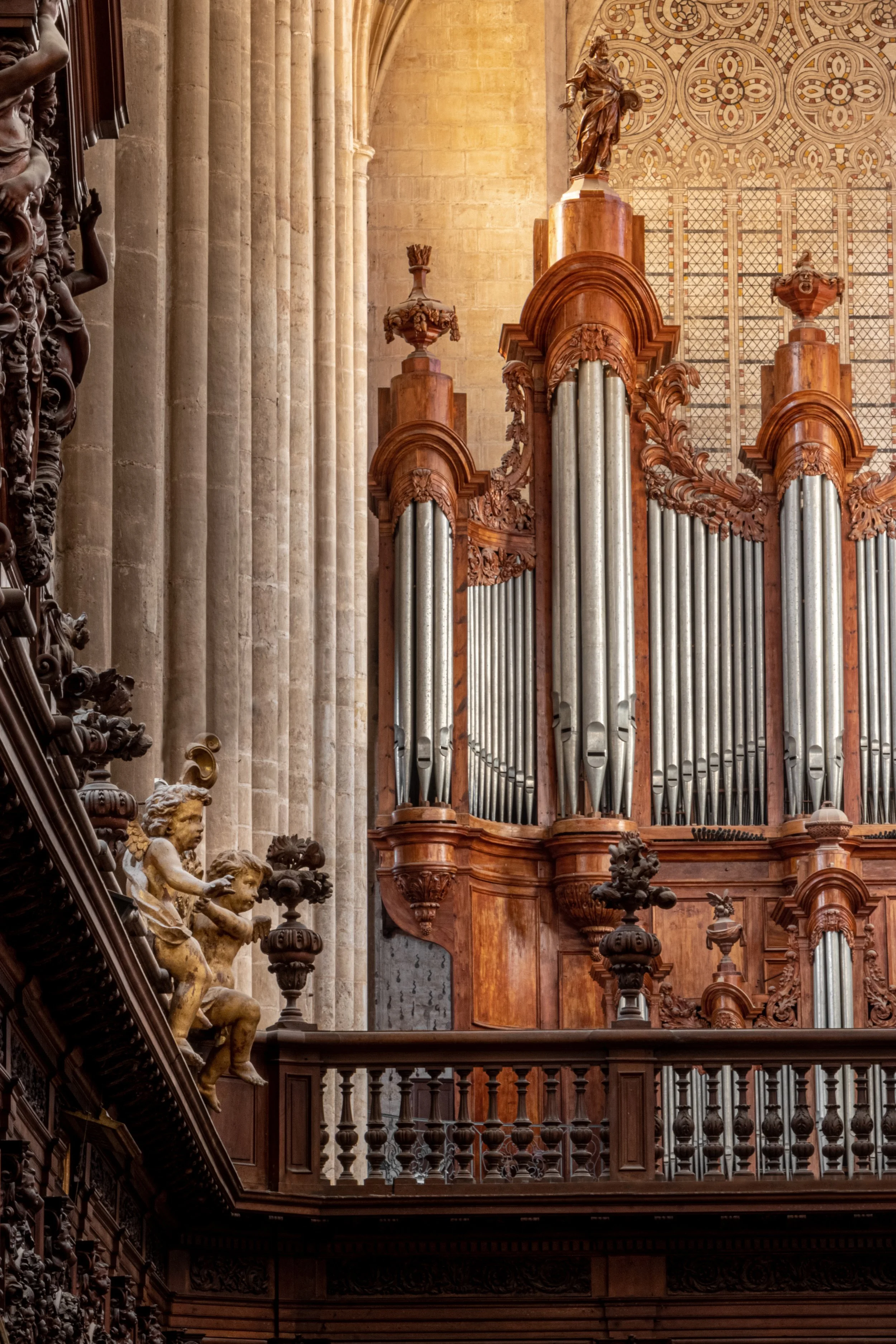 Un orgue en bois avec de nombreuses tuyaux en métal dans une église ou une cathédrale, avec des sculptures en bois et des colonnes en pierre en arrière-plan.