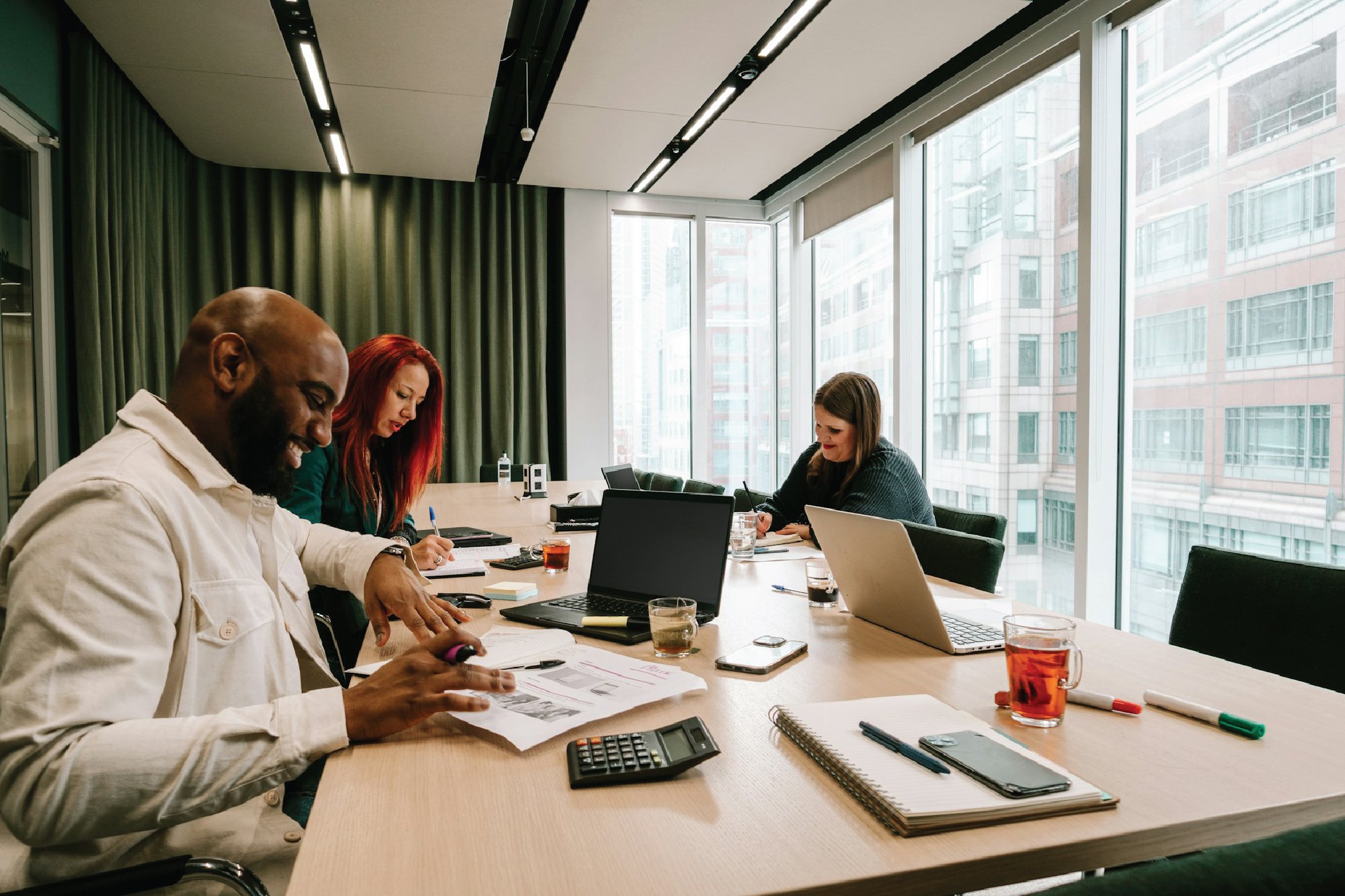 A diverse group of four people having a meeting in a modern office conference room with large windows and city views.