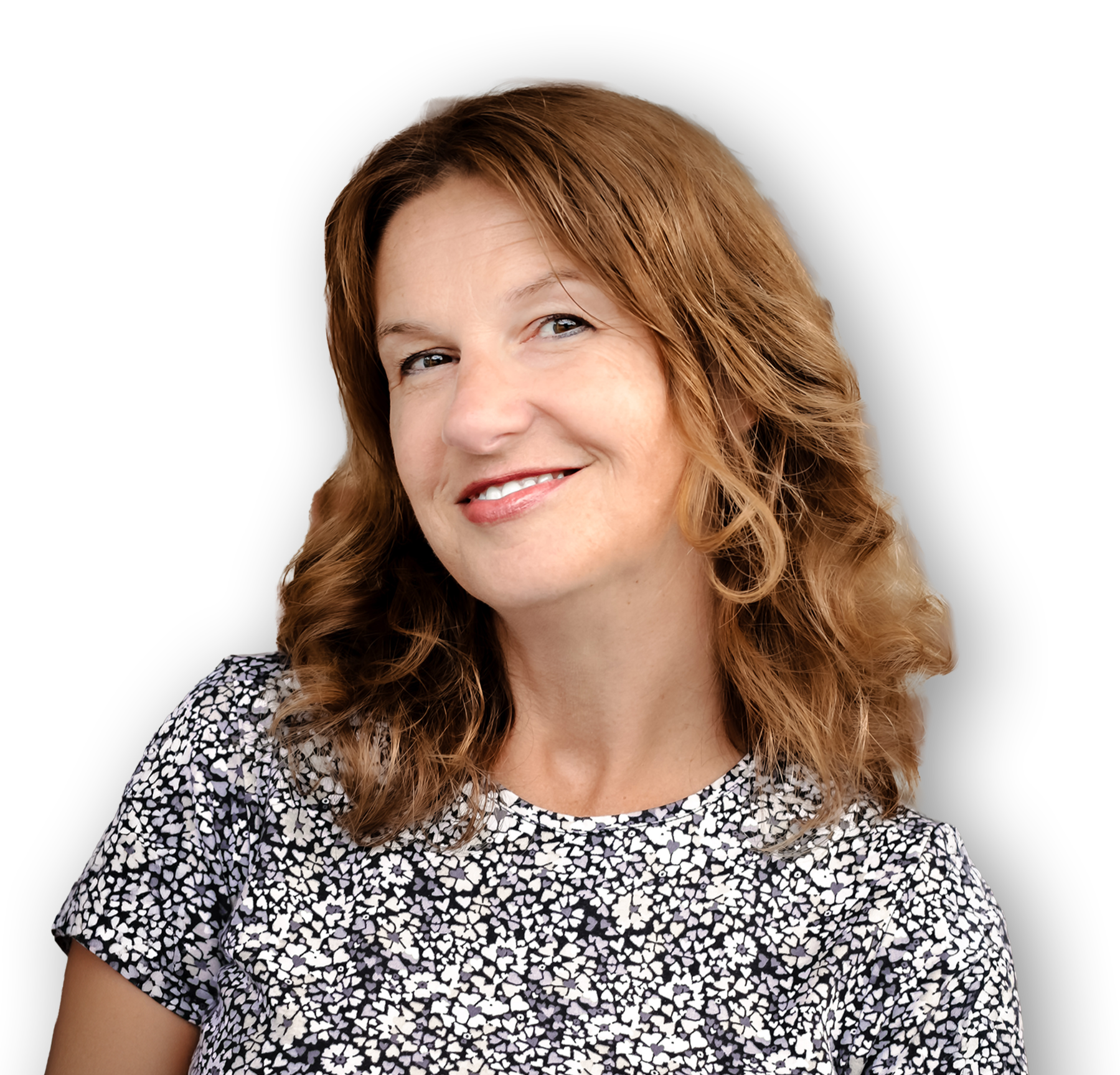 A woman with long, wavy red hair and fair skin, smiling, wearing a black and white floral patterned top, against a black background.