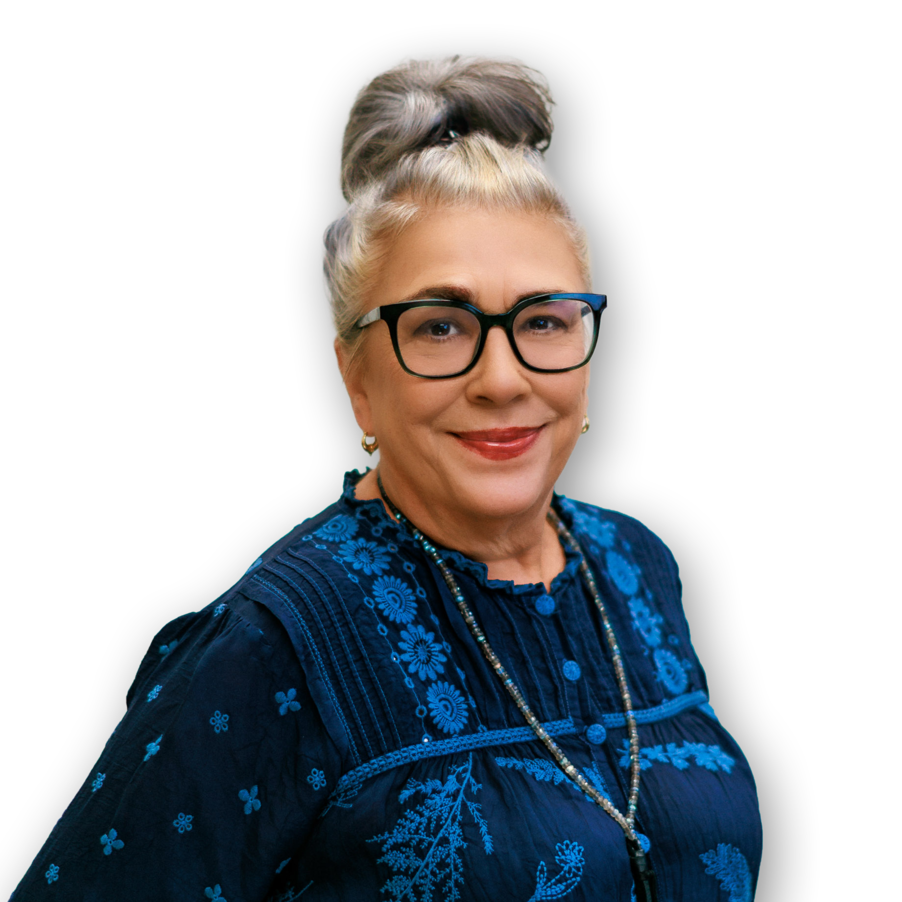 Close-up of a woman with glasses, wearing a blue embroidered top and jewelry, smiling against a black background.