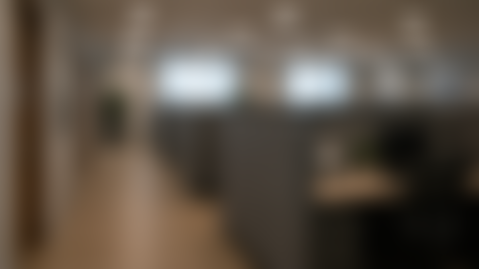 Blurred interior of a modern office or living space with large windows, some furniture, and a wooden floor.