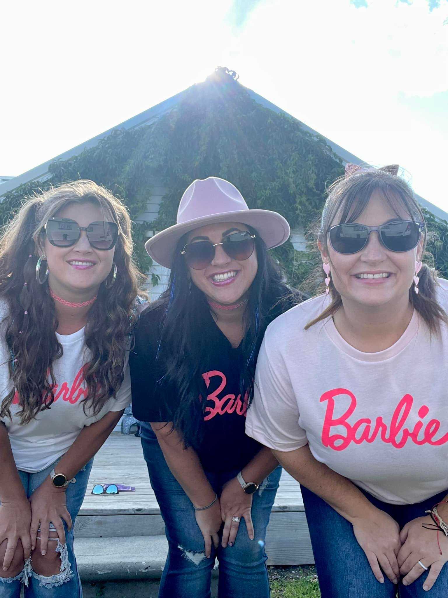 Three women smiling outdoors in front of a large, steep, green-covered mountain or volcano with a bright sky.
